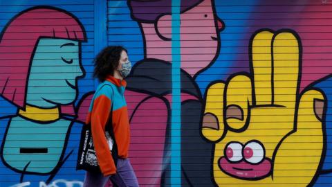 A woman wearing a mask walks past a mural in Manchester