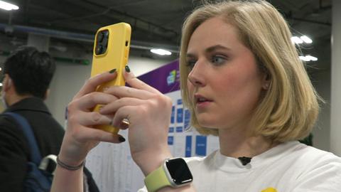 Rebecca Rosenberg, CEO and founder of ReBokeh looks at her yellow iPhone. She is wearing a watch with a yellow strap.