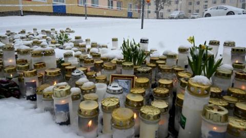Candles and flowers are laid on the ground in the snow at Viertola school in Vantaa, Finland.