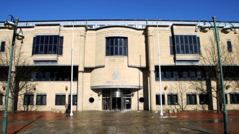 Library image showing the outside of Bradford Crown Court. It is a beige building, with three large windows on the upper level and a number of smaller square windows and a revolving door on the ground level.