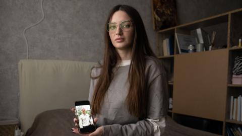 Julia Hripun sitting in her bedroom with a picture of her captive father on her iPhone