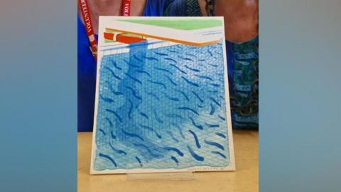 A colourful blue print of a swimming pool, with a faint pencilled signature of David Hockney in the bottom right hand side