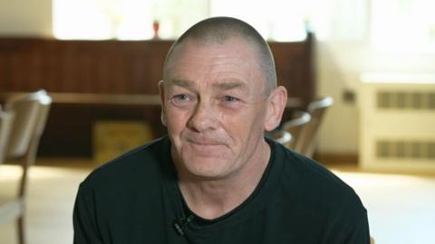 Grant Calder smiling and looking slightly off-camera, wearing a black t-shirt with short hair.