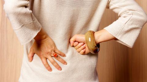A woman wearing a beige top holds her hands to her lower back