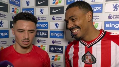 Two footballers stand for post-match press conference. One, Wilson Isidor, smiles as he looks at the interviewer