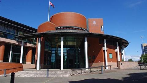 The exterior of a dark brown brick court building with a large glass front door area. 