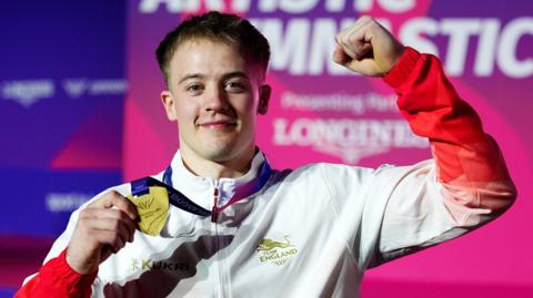 Luke Whitehouse raises his right arm and shows off his gold medal