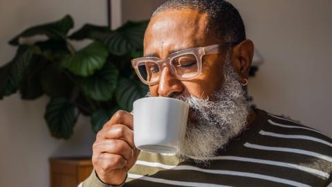 An older gentleman sips from a white coffee mug.