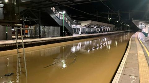 A train station with brown water completely submerging the track area.