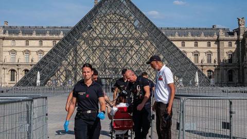 Firefighters from the Paris Fire Brigade escort a person outside the Louvre Museum during an intense heatwave on 25 June 2026