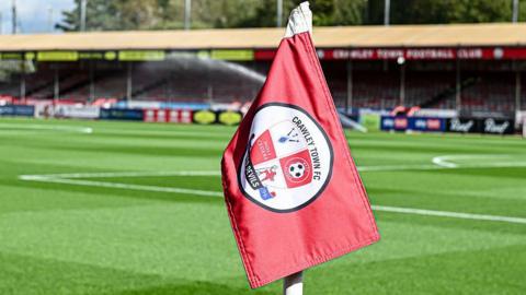A red corner flag with Crawley Town branding, with Broadfield Stadium's pitch in the background