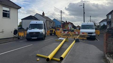 Two yellow poles laid on the tarmac in front of a construction site with two white vans parked either side
