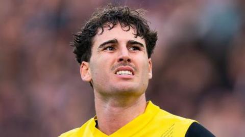 Matthew Garbett looks up while wearing a yellow football shirt
