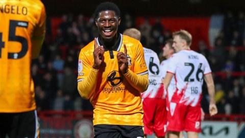 A smiling Sullay Kaikai points upwards with both index fingers after scoring for Cambridge United against Stevenage last October