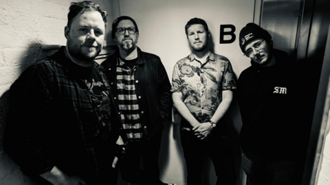 A black and white picture of the four members of Sinews in a corridor, posing for a band photo.