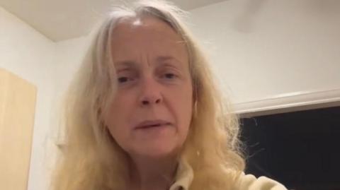 A woman in her 50s with blonde hair looks at the camera
