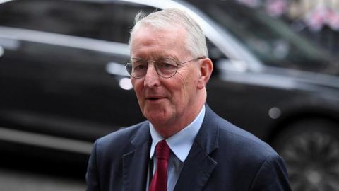 Hilary Benn pictured in London in July. He is wearing glasses, a dark blue jacket, a blue shirt and a red tie