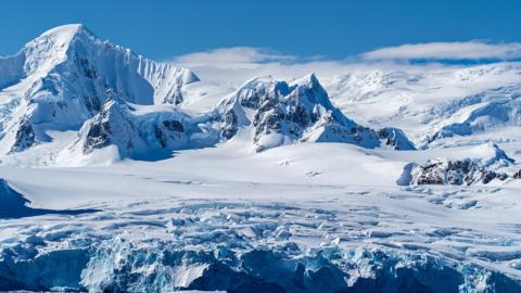 A snowy landscape of Antarctica. You can see snow and ice in the foreground and snowy mountains in the background