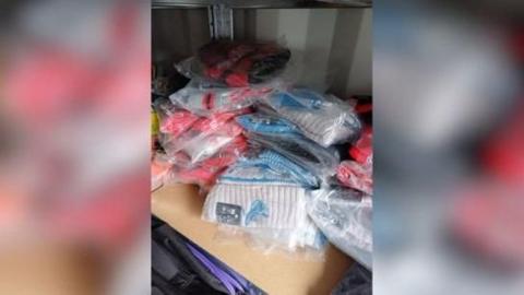 Dozens of woolly hats with NFL branding sit on a table, still in plastic packaging. Some are grey and blue, while others are red.