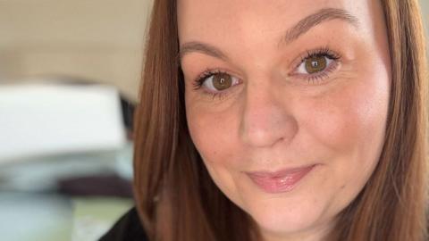 A selfie of Symone, who has brown hair and brown eyes and is smiling at the camera.