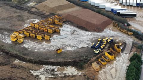 A drone image of the former Greyhound stadium with muddy ground and several yellow rubbish skips on it.