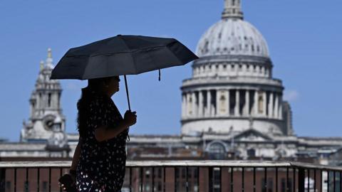 A woman walks under an umbrella past St Paul's Cathedral in London during the heatwave.