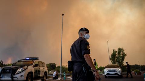A Civil Guard officer wears a protective mask as smoke from a wildfire obscures the sky in Cenicientos, Madrid
