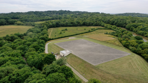 A drone image of an Essex and Suffolk Water's partially underground reservoir. It is surrounded by vast green forest. 