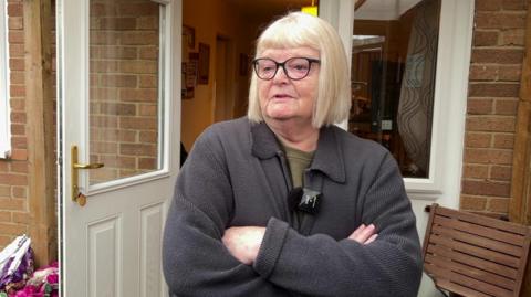 Frances Ward, a woman with short blonde hair standing in her back garden with her arms crossed. Behind her, the door to her house is open