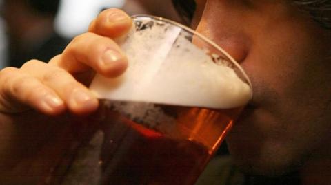 File photo of someone drinking from a pint glass of beer. Other people are just visible behind.