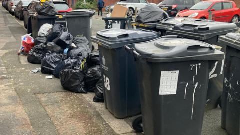 Bins in Warrington with rubbish bags on the floor next to them