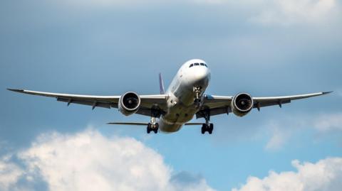A stock photo of an airplane taking off. The sky is blue and sunny with some clouds.