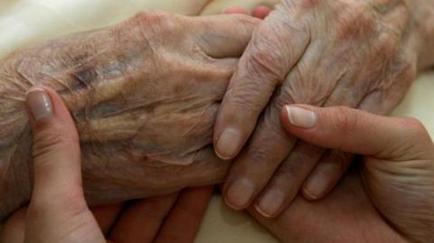 A young carer holds the hands of an older woman 