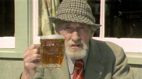 Fyfe Robertson sits outside and holds up a pint