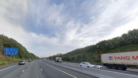 Motorway with traffic on both sides of the carriageway and blue road sign to the left.
