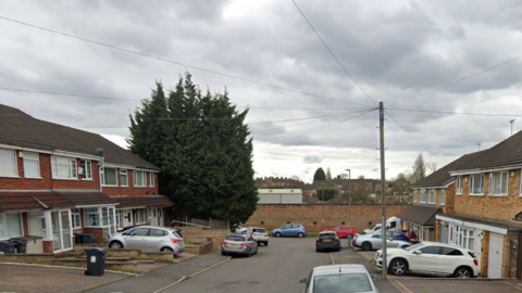 Houses can be seen on either side of the cul de sac with cars parked on drives and on the street