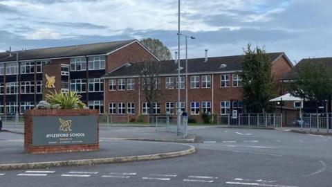 General view of buildings and a wall with the words Aylesford School and a motif of a bird.