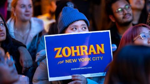 Mamdani supporter watches his speech holding 'Zohran' placard