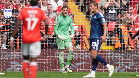 Leicester City's Jakub Stolarczyk opens his mouth wide and roars whilst pumping his fists down by his hips as he stands in goal wearing a green top and shorts.