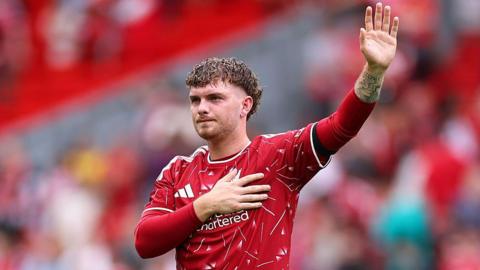 Harvey Elliott clasps the Liverpool badge with his right hand while raising his left arm
