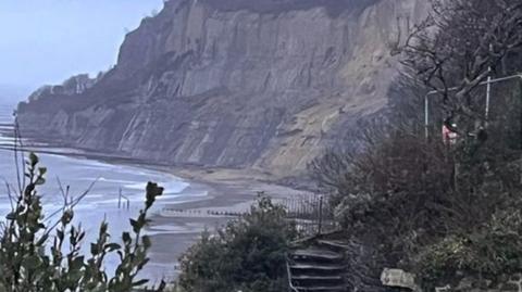 A beach with grey cliffs. It looks like the tide is in. In the foreground, there are some steps.