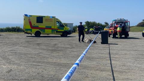 Police tape, and ambulance and fire service vehicle, plus several emergency services vehicles.