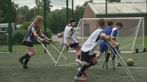 Young people using crutches playing football.