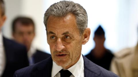 A headshot of Nicolas Sarkozy, wearing a dark blue suit jacket