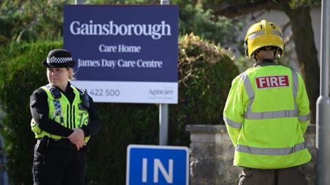 A police officer and emergency worker stand beside a sign for Gainsborough Care 91ȱ in Dorset