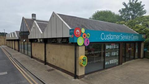 The building is made of sand-coloured stone and features a glass front and sign above the entrance that reads "customer service centre"