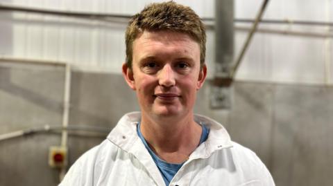 Man in white coat looks directly at camera in his abattoir