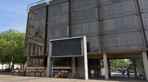A five-storey, glass-fronted office building in a pedestrianised square.