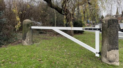 A clean white wooden gate stands flagged either side by large stone pillars. 