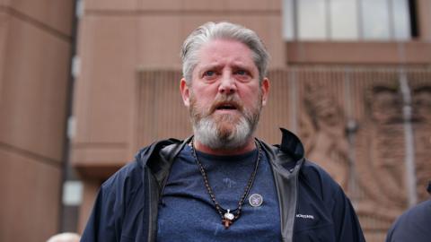 Tim Edwards, who has grey hair swept backwards and a grey beard, speaks to the camera outside Liverpool Crown Court with a serious, angry expression on his face